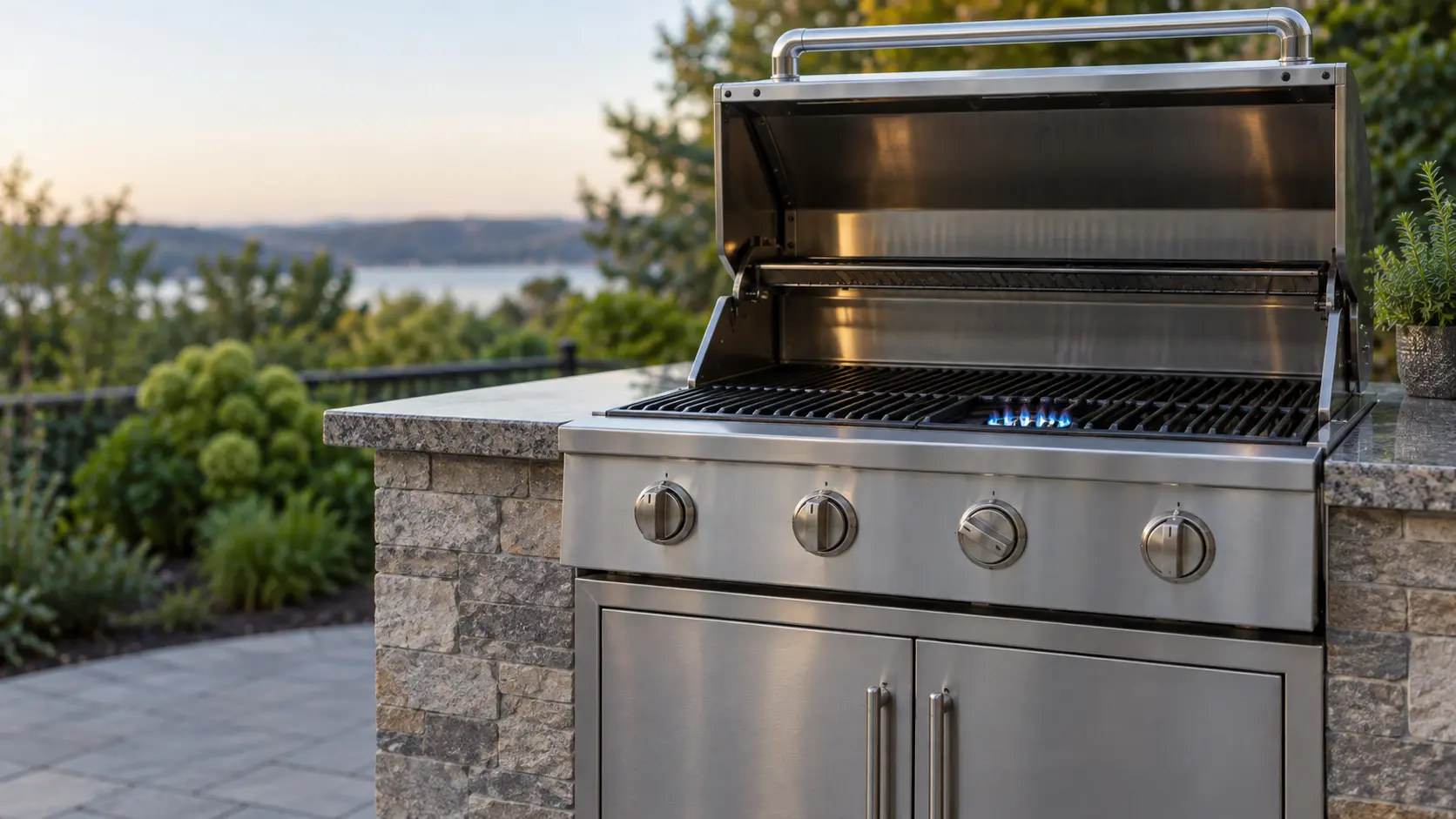 A built-in stainless grill head in a stone island with its lid up, one burner still showing a small blue flame while its knob on the panel points to off, the other burners dark, the cabinet doors below closed.