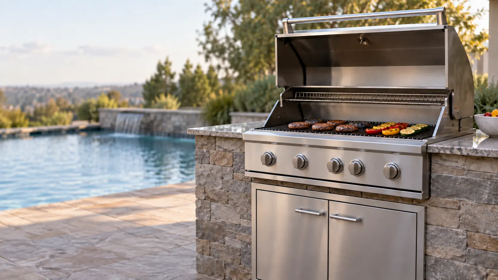 A family backyard with a stainless built-in grill by the pool, seen from across the patio.